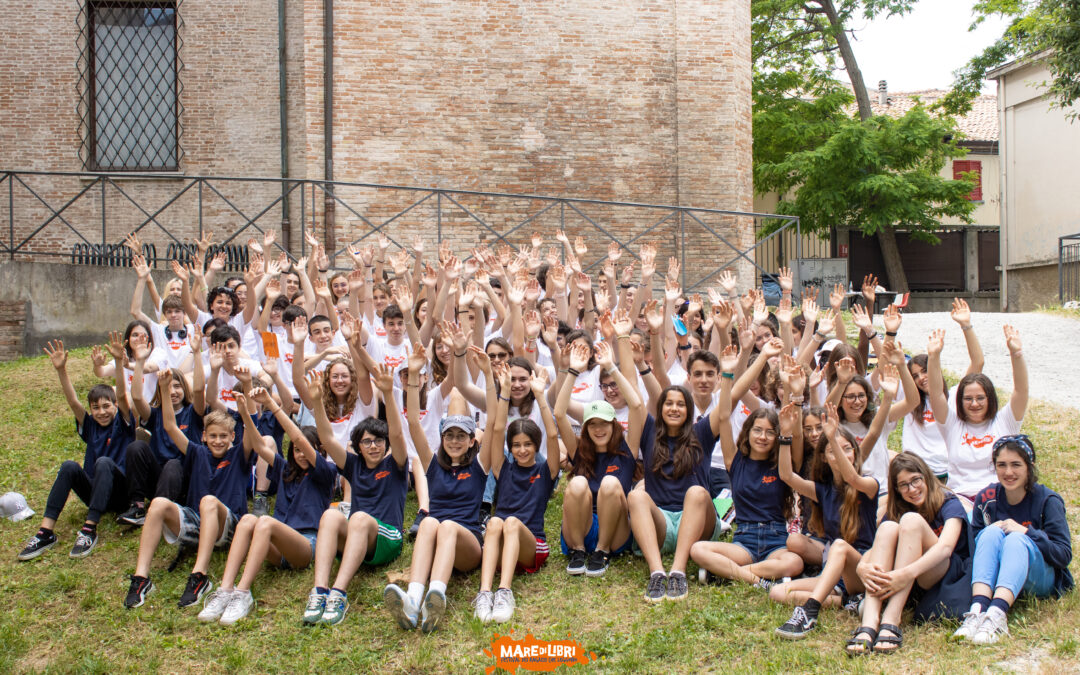 Grande gruppo di ragazzi e ragazze volontari di Mare di Libri sul prato e con le braccia alzate
